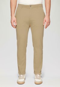 Beige chino's met een slim fit, met een vlakke voorkant, twee voorzakken en een knoopsluiting. Gestyled met witte en beige sneakers.