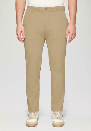Beige Chinos in schlanker Passform mit flachem Bund, zwei vorderen Taschen und Knopfverschluss. Kombiniert mit weißen und beigen Sneakers.