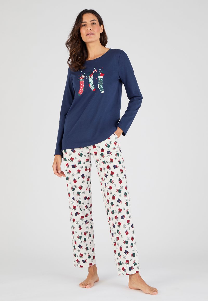 Camiseta de manga larga navy con gráfico de calcetín festivo; pantalones blancos con patrón de regalos y copos de nieve en rojo, verde y negro. Material de algodón, corte relajado.