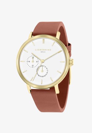 Montre en métal doré avec un cadran blanc, deux sous-cadrans et un bracelet en silicone couleur rose. Caractéristiques : marqueurs d'heure minimalistes et lunette texturée.