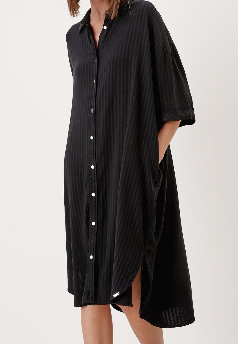 Czarna sukienka koszulowa w paski z krótkim rękawem, z guzikami z przodu, bocznymi kieszeniami i luźnym krojem. Gładka tekstura z długością do kolan.