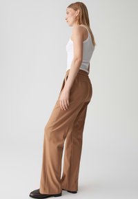 Pantaloni a vita alta marrone chiaro con una vestibilità rilassata, realizzati in tessuto morbido, dotati di una vita elastica e tasche laterali.