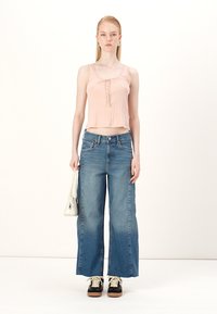 Pink sleeveless top with lace details, high-waisted light blue wide-leg jeans, black sneakers, and a white bag.