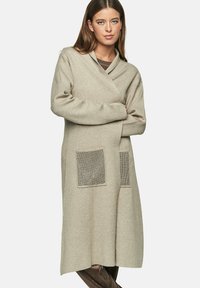 Beige lange cardigan gemaakt van zacht materiaal, met een schuilkraag, twee gestructureerde opgestikte zakken en een ontspannen pasvorm.