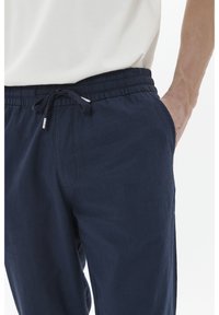 Pantalones de corte relajado en azul marino, hechos de una tela texturizada, que cuentan con una cintura elástica con cordón y bolsillos laterales.