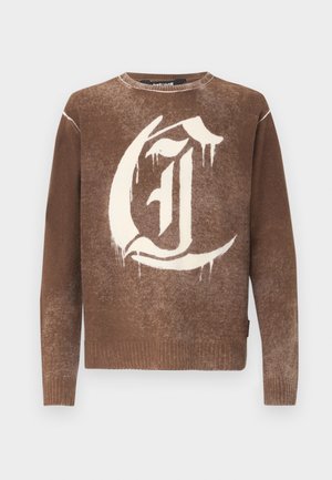 Rudas kraklio megztinis su dideliu baltu stilizuotu gotikos raide "C" priekyje ir su raukšlėtomis rankovėmis bei apatine dalimi.