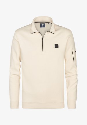 Kremowy pulower z kołnierzem typu stójka i półsuwnym zapięciem. Posiada czarną kwadratową naszywkę oraz kieszeń na rękawie zapinaną na zamek. Wykonany z miękkiego dzianinowego materiału.