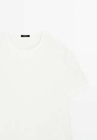 Hvid bomulds t-shirt med korte ærmer og rund halsudskæring, med en glat tekstur, der har et lille sort mærke ved halsen.