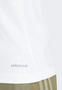 White athletic shirt featuring a textured design, mesh panels, and "AEROREADY" branding near the hem. Suitable for active wear.