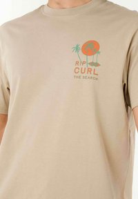 Camiseta de algodón beige con un diseño gráfico de palmeras y un sol en color naranja y verde. De manga corta y estilo de cuello redondo.