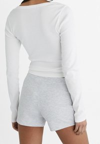 Un haut à manches longues blanc côtelé associé à un short court léger et doux de couleur gris clair. La tenue présente une coupe ajustée et des accents minimaux.