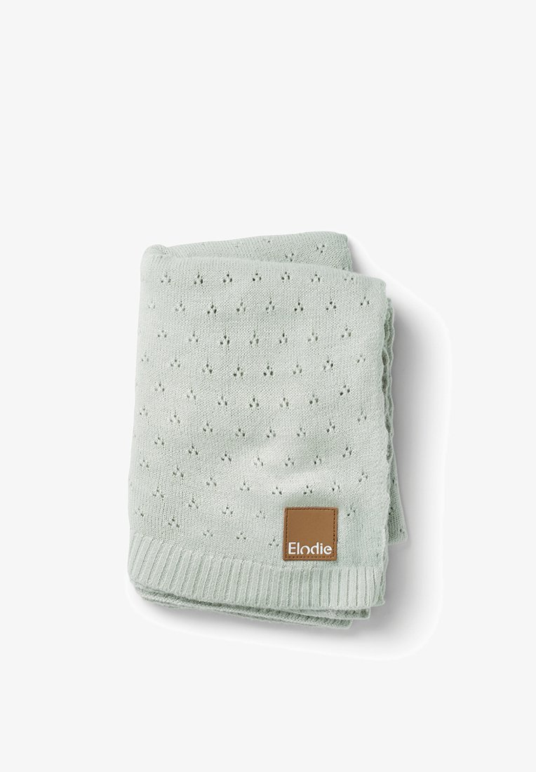 Coperta lavorata a maglia di colore verde chiaro piegata, con un piccolo motivo ad occhiello e un'etichetta in pelle marrone con la scritta "Elodie" su sfondo bianco.