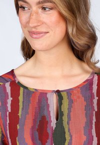 Bunt gemusterter Oberteil mit Zickzackstreifen in Rot, Lila, Grün und Orange. Schlüsselbund-Detail am Kragen mit einem kleinen Knopfakzent.