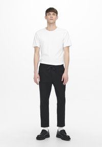 Witte t-shirt met korte mouwen en zwarte joggingbroek met trekkoord. De broek heeft een tapered leg ontwerp, aangevuld met zwarte veterschoenen.