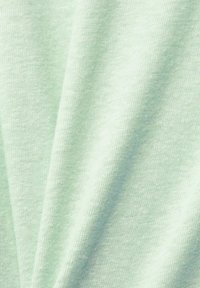 Tissu doux vert clair avec une texture tricotée visible et de légers plis créant des ombres et des reflets.
