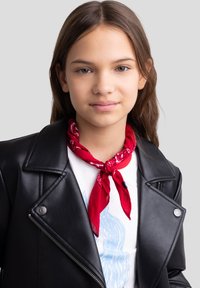 Foulard rosso annodato intorno al collo, indossato con una giacca di pelle nera con dettagli in argento e rever a punta. T-shirt bianca sotto.