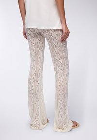 Pantaloni bianchi a maglia con un motivo testurizzato e aperto a forma di diamante. I pantaloni sono svasati sul fondo e abbinati a sandali beige.