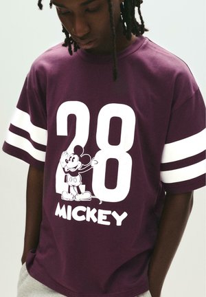 Lilla bomulds T-shirt med korte ærmer, hvide striber, stor hvid "28" og et grafik af Mickey Mouse med teksten "Mickey" nedenunder.