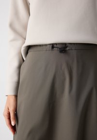 Falda de tela gris con una textura suave, que presenta una cintura con cordón ajustable y un diseño minimalista. Parte superior de color beige claro visible arriba.