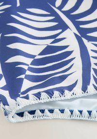 Blau-weißer Stoff mit einem markanten Blättermuster und einem weißen Fransenbesatz am Rand.