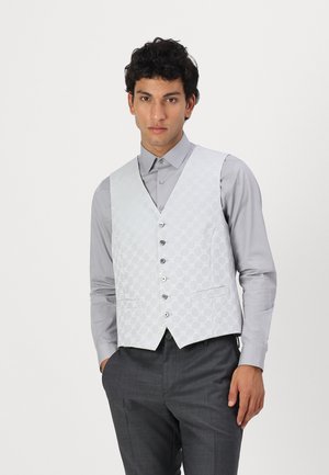 Gilet gris clair avec un motif matelassé, six boutons et deux poches avant, porté par-dessus une chemise grise assortie et un pantalon charbon.