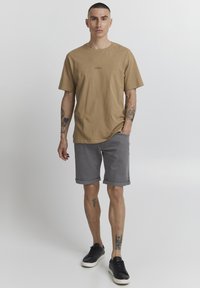 Tan cotton t-shirt with short sleeves and crew neck, paired with gray shorts. Black sneakers complete the outfit.