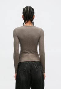 Hnědý žebrovaný top s dlouhými rukávy, přiléhavého střihu a kulatým výstřihem, spárovaný s černými džíny s vysokým pasem a vyšívanými detaily.