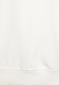 Tissu de sweat-shirt blanc avec une texture subtile, présentant un ourlet côtelé. Aucune motif ni embellissement visible.