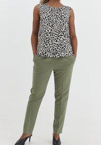 Sleeveless top in a black and white leopard print, paired with olive green tailored pants and black high-heeled shoes.