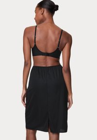 Set di lingerie nera con spalline regolabili e chiusura posteriore, abbinato a una gonna nera con spacco laterale e vita arricciata.
