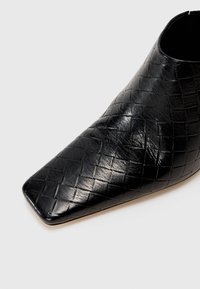 Zwarte leren enkellaars met een geweven structuur, vierkante neus en gladde afwerking. Licht gebogen bovenwerk met een slank silhouet.