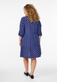 Navyblå kjole med polkaprikker, trekvartærmer, samlet talje og lagdelt skirt. Stof ser let og blødt ud.