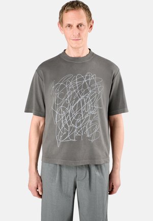 Camiseta gris de manga corta con un diseño abstracto de líneas blancas en la parte frontal. Cuello redondo, corte relajado, fabricada en suave material de algodón.