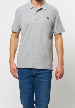 Polo gris à manches courtes avec col et petit logo marine, assorti à un jean bleu. Le tissu semble doux avec une finition texturée.