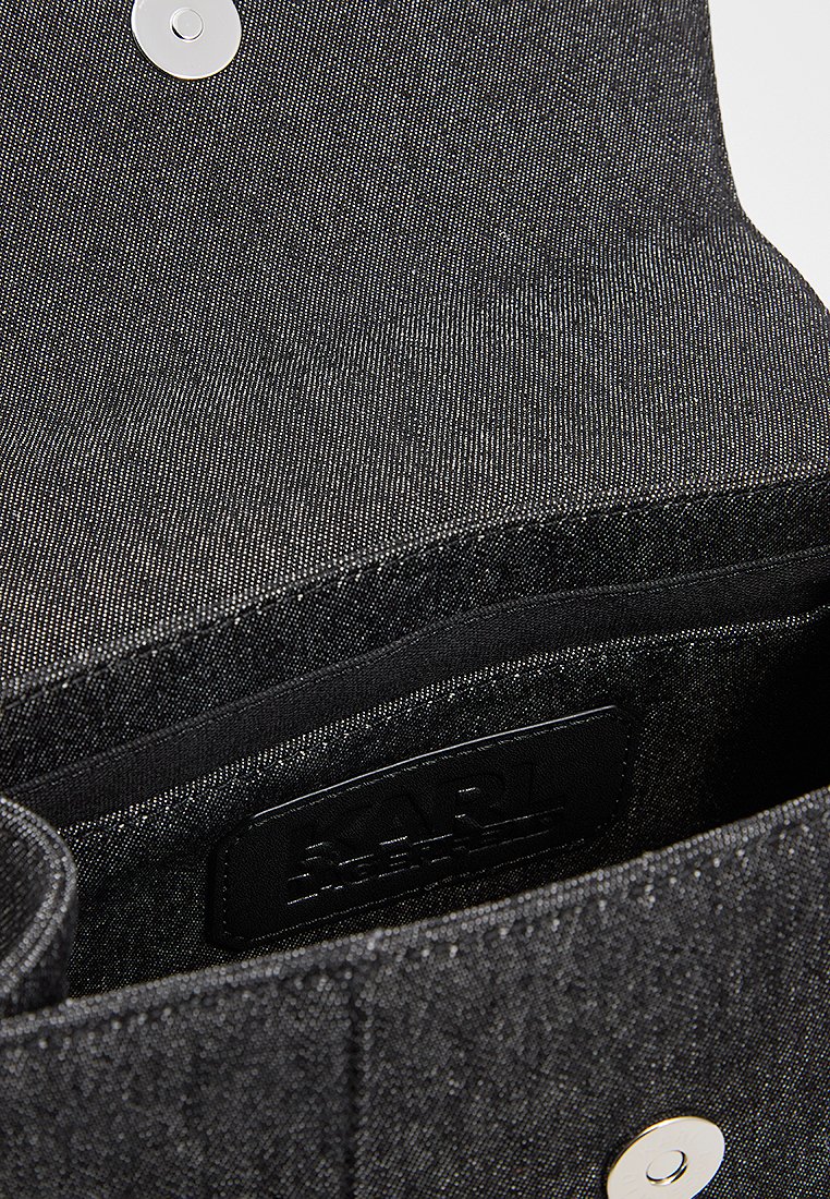 Intérieur d'un sac en denim noir avec une texture lisse, featuring un patch logo et un fermoir à pression argenté. Design simple et fonctionnel.