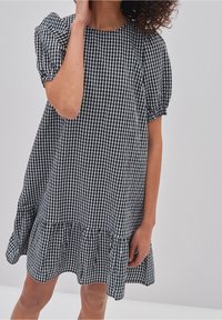 Svart och vit rutig klänning med puffärmar, rund halsringning och en svängd volangnederdel. Gjord av lätt tyg, den har en loose fit.