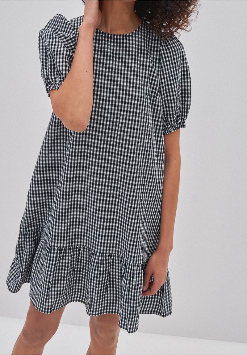 Svart och vit rutig klänning med puffärmar, rund halsringning och en svängd volangnederdel. Gjord av lätt tyg, den har en loose fit.
