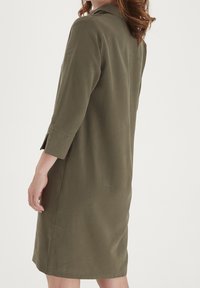 Robe vert olive à manches longues, col à revers, et coupe décontractée, avec des fentes aux poignets et une longueur au genou. Texture lisse.