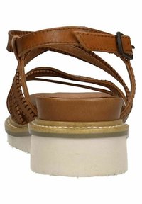 Sandali in pelle marrone con cinturini incrociati, suola chiara e una piattaforma leggermente sollevata. Dettagli testurizzati sui cinturini. fibbia regolabile.