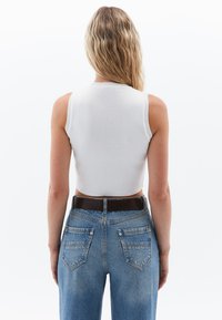 Top a sfondo bianco in cotone rigato, senza maniche, con spalline larghe, abbinato a jeans in denim blu a vita alta e una cintura marrone. Cuciture visibili e tasche posteriori.