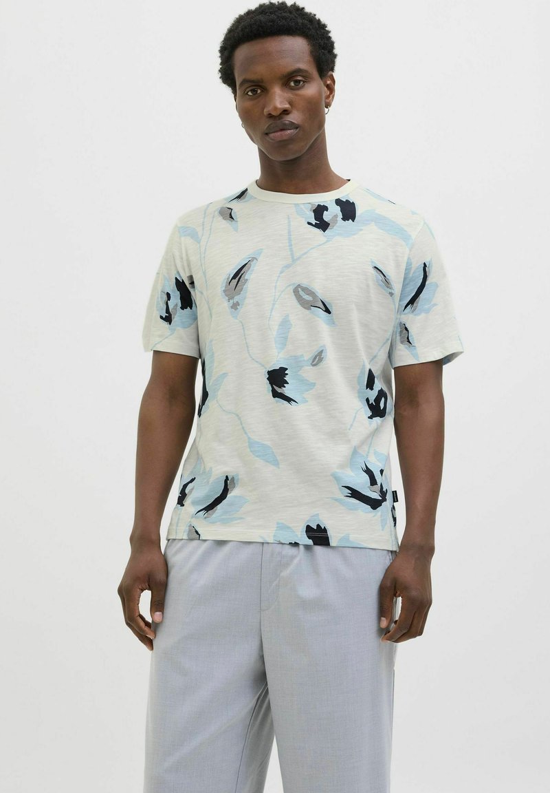 Camiseta de manga corta de color claro con un patrón floral en tonos azules y negros. Hecha de tela suave, con escote redondo y un fit relajado.