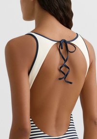 Achteraanzicht van een persoon die een marineblauw-wit gestreept badpak draagt met een open rug en een striksluiting aan de bovenrug.