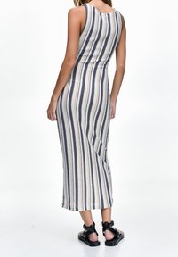 Robe maxi rayée avec une silhouette ajustée en couleurs crème et marine, dotée d'une texture tricotée et d'un design sans manches. Sandales noires complètent le look.