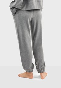 Pantalones de chándal grises hechos de material suave, con puños elásticos, bolsillos laterales y un ajuste relajado. Costuras visibles y textura suave.
