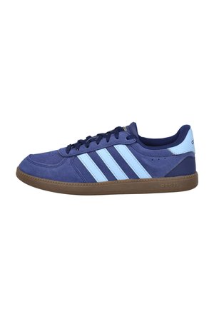 Zapatilla baja Adidas azul marino con tres rayas azul claro, cordones negros y suela de goma marrón, vista lateral sobre fondo blanco.