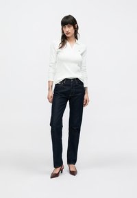 Biela polokošeľa s dlhým rukávom, tmavomodré rovné džínsy a bordové lodičky na podpätku. Jednoduchý dizajn, málo viditeľných detailov, hladký povrch.