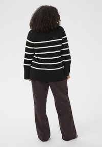 Black and white striped knitted sweater with a loose fit, featuring long sleeves and a ribbed hem, paired with dark purple wide-leg pants.