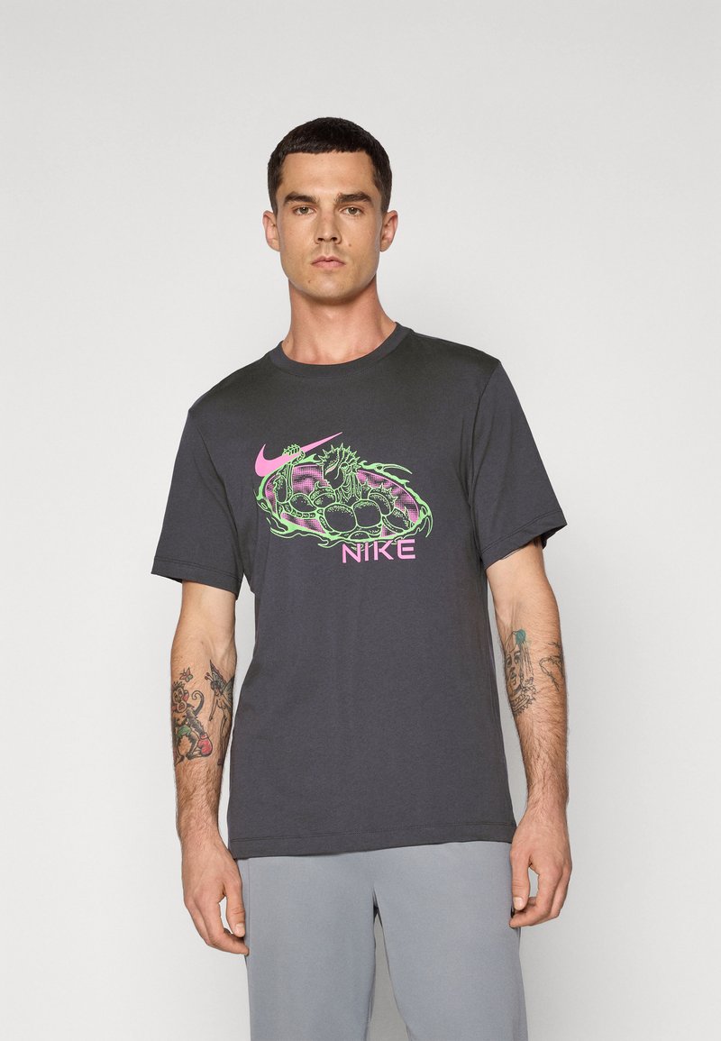 Mørkegrå bomulds-T-shirt med et farverigt grafisk motiv af et væsen og Nike-logoet i pink og grøn. Den har korte ærmer og rund halsudskæring.