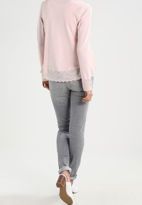 Ljusrosa ribbad stickad topp med spetsdetalj i nederkant, kombinerad med uppvikta grå jeans och vita klackar. Utan visar en avslappnad stil.