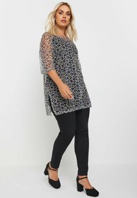 Gennemsigtig leopardprint-top med korte gennemsigtige ærmer, rund halsudskæring, sideslidser og parret med sorte tætsiddende jeans og sorte hæle.